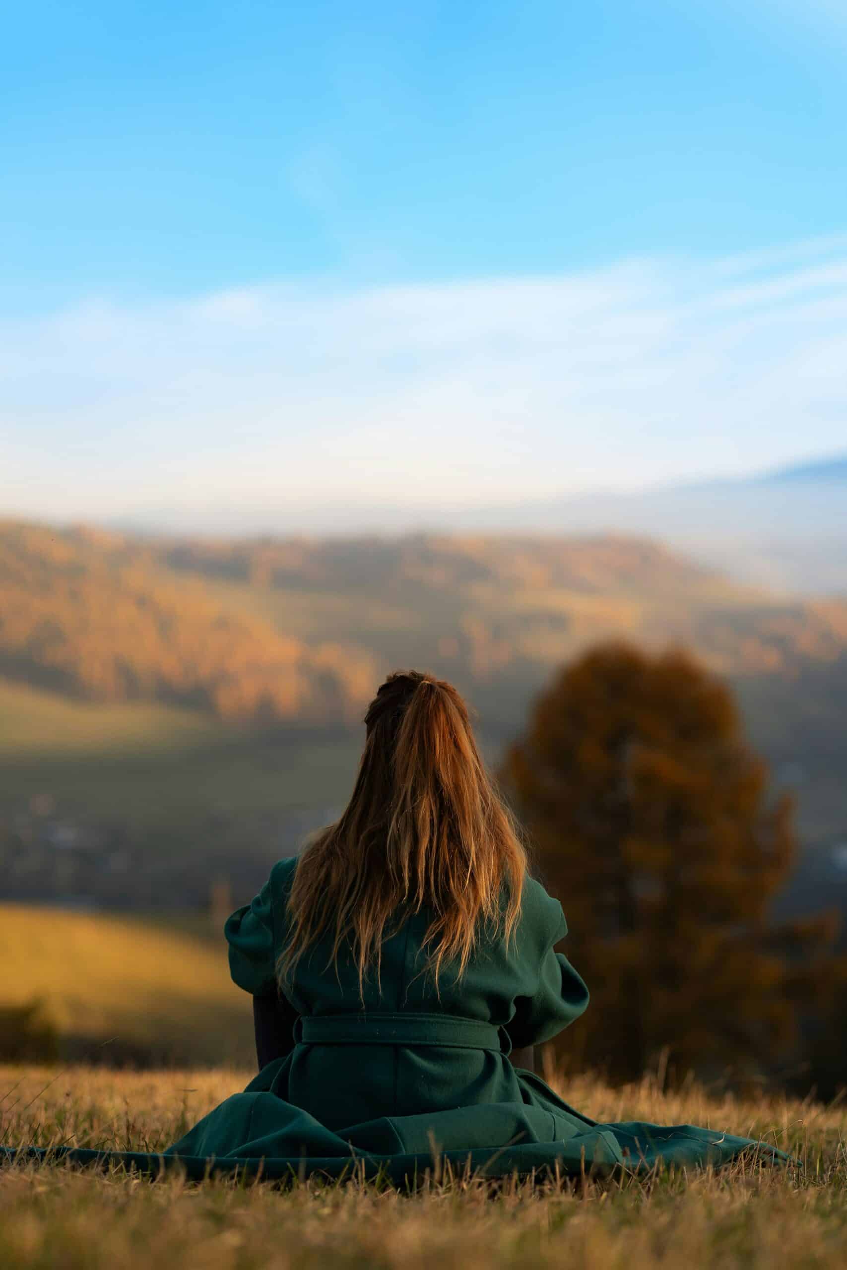 Woman sitting on a hillside gazing over an autumn valley, representing self-reflection and healing